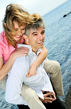 Smiling couple having fun outdoors after successful dental implant procedure in Denver