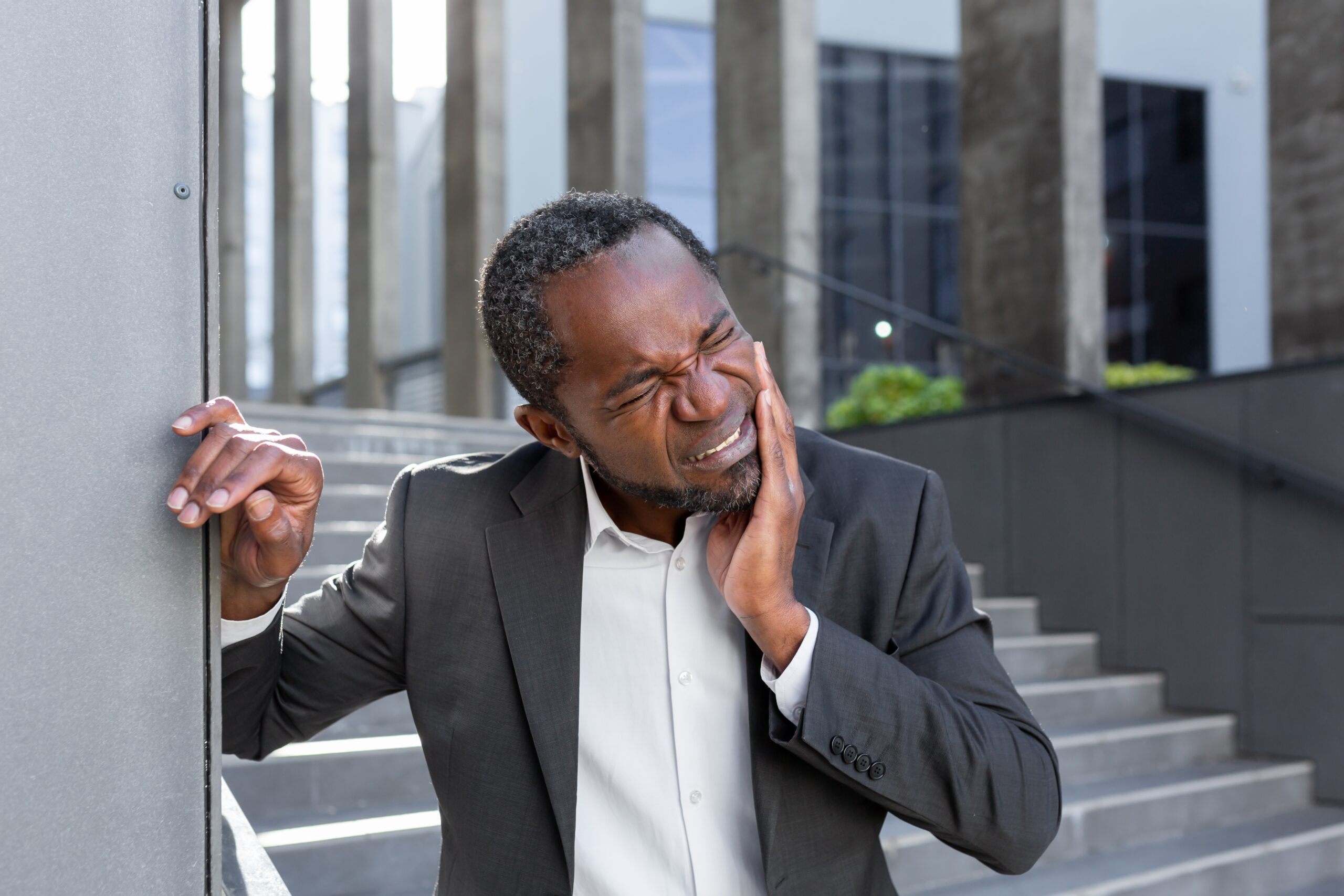 man in a suit outside an office park suffering from severe tooth pain