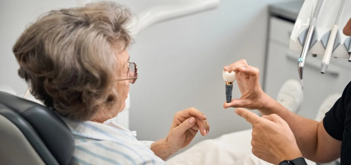 Doctor shows a model of dental implant to elderly lady in Denver