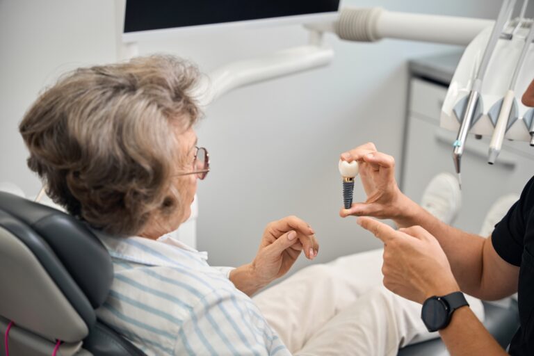 Doctor shows a model of dental implant to elderly lady in Denver