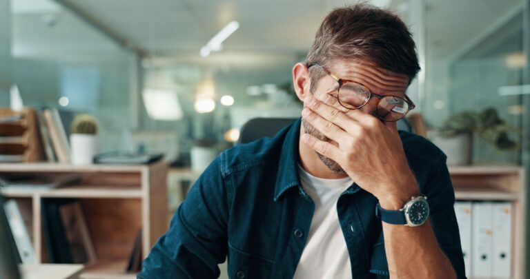 man suffering from a headache, covering his face with his hand