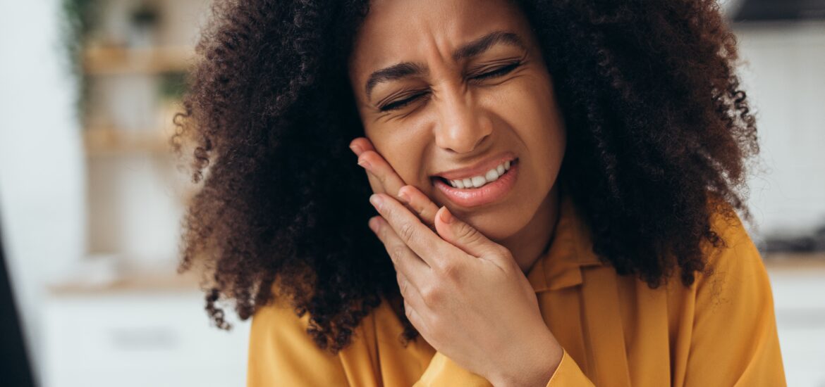 young woman in yellow shirt holding jaw, severe tooth pain