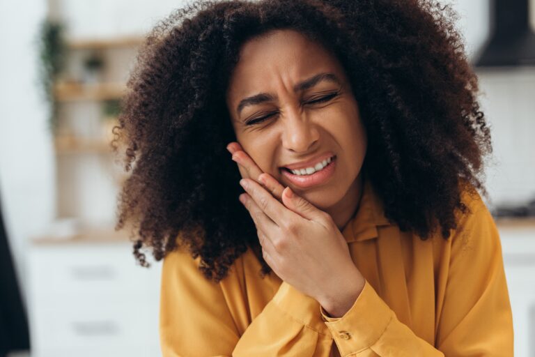 young woman in yellow shirt holding jaw, severe tooth pain