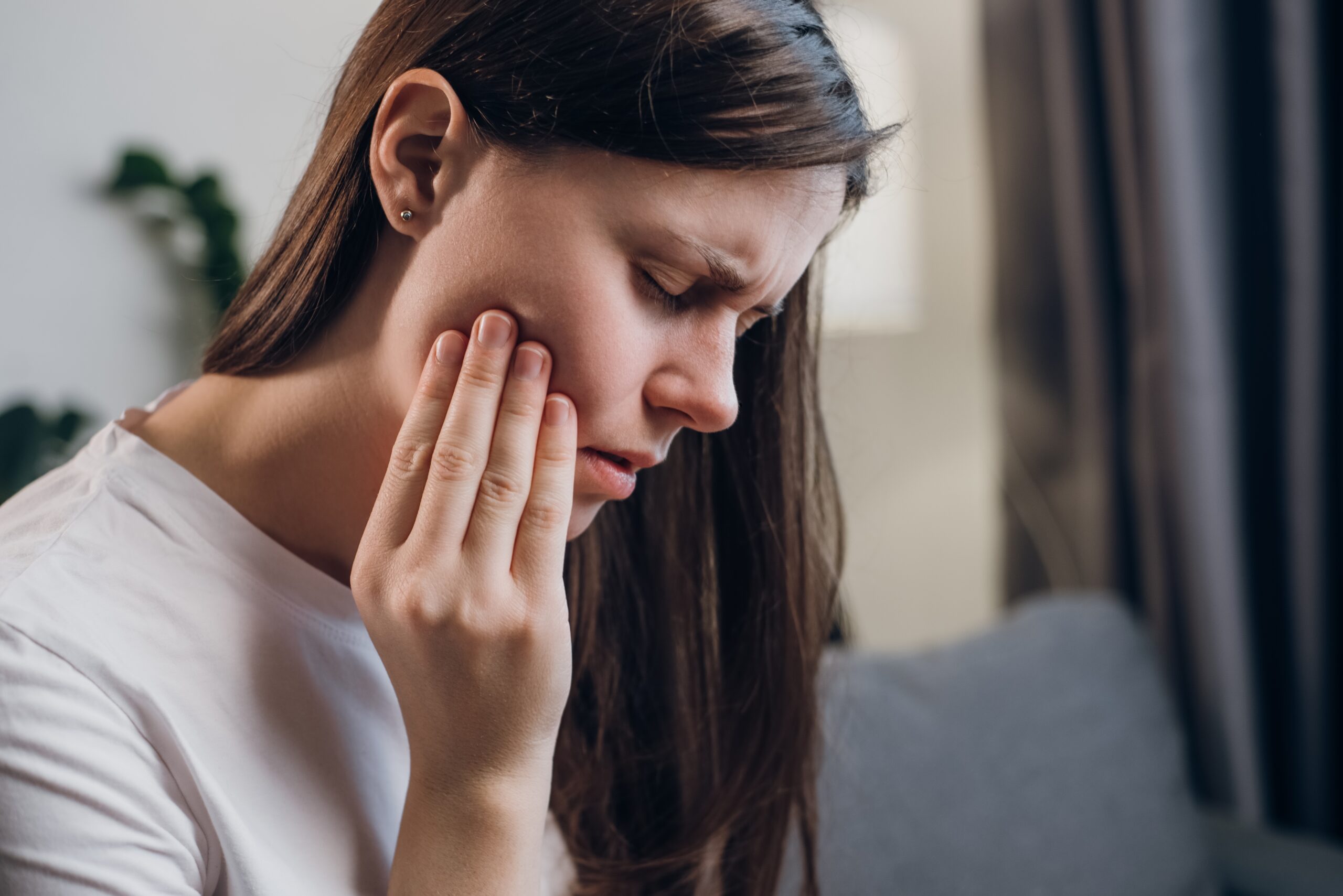 young woman with her hand on her jaw, wisdom tooth pain